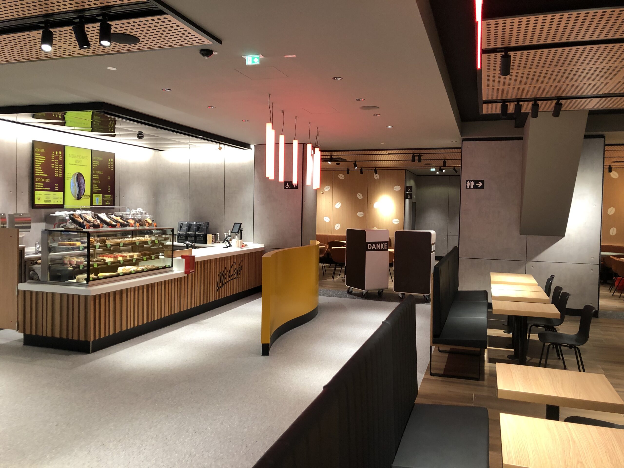 McCafé counter area with recessed downlights in a clean white ceiling and warm pendant lights