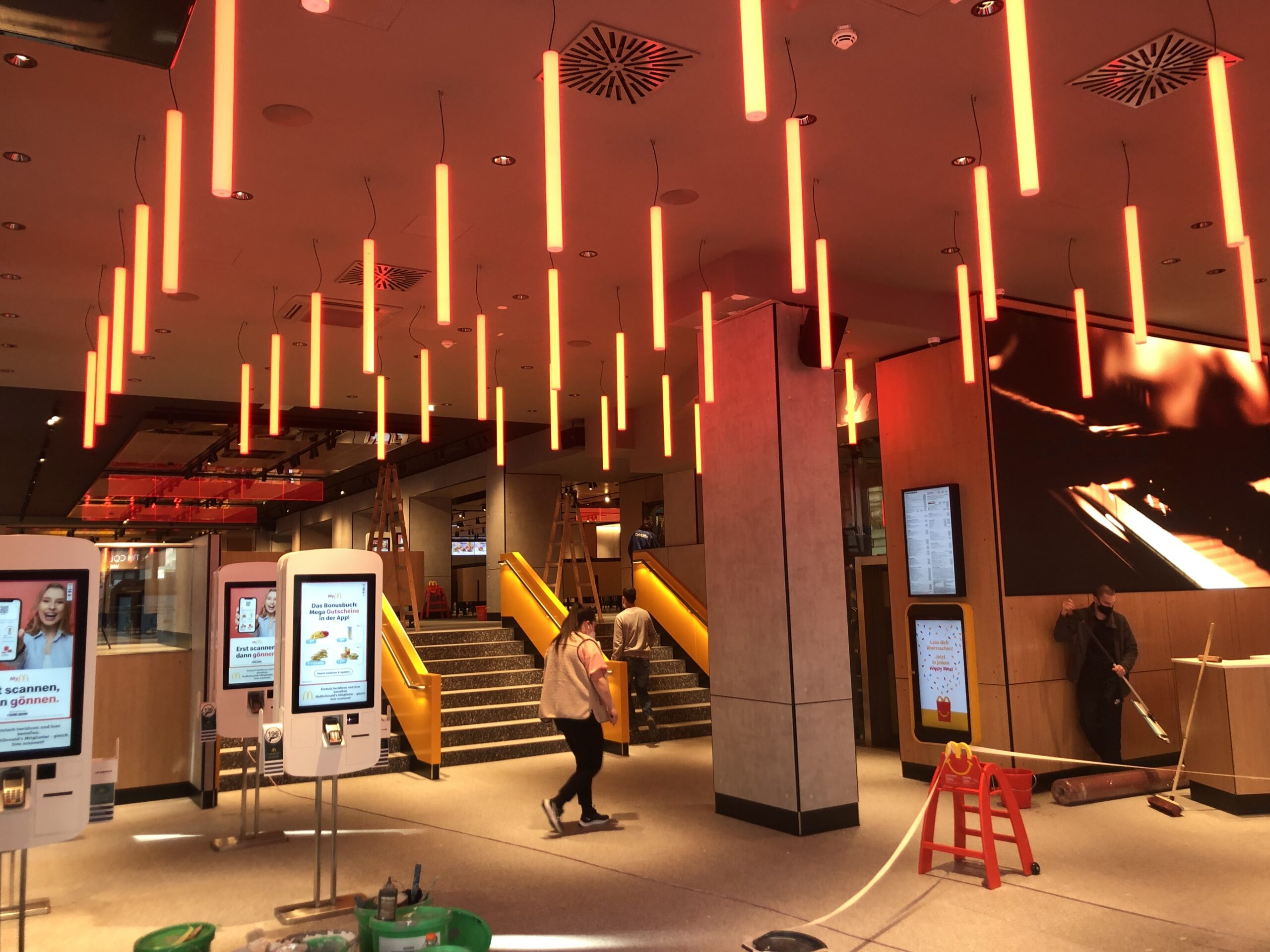 Field of warm orange cylindrical pendant lights across a McDonald's dining ceiling