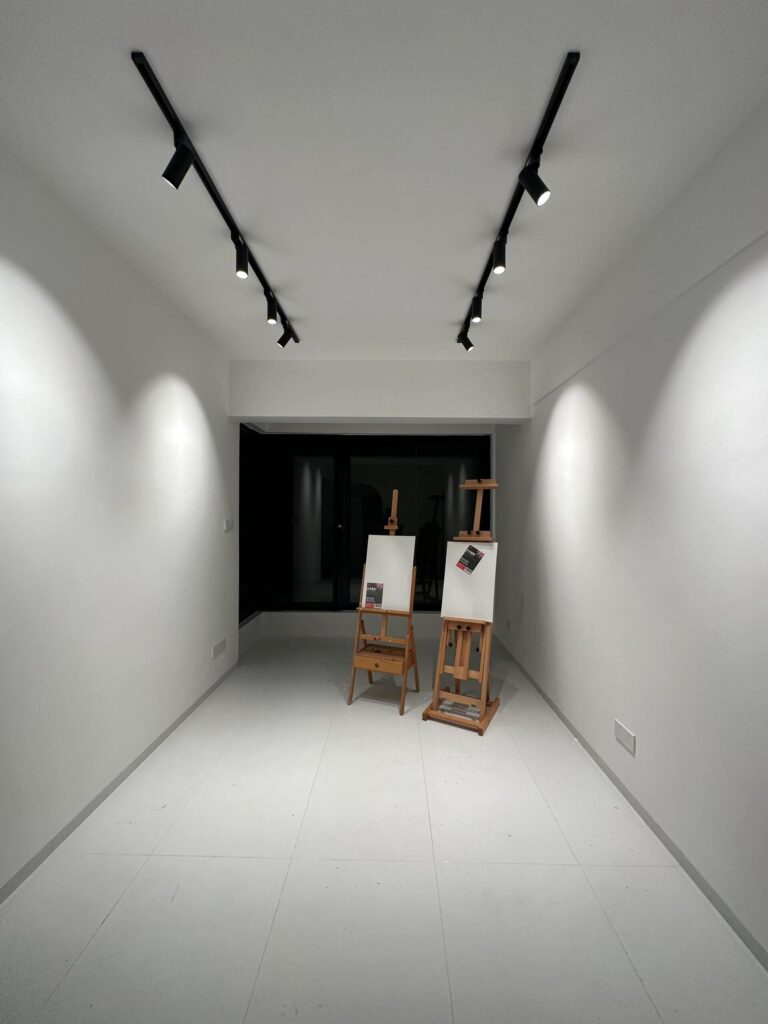 Minimalist studio with dual black track lights in V-arrangement creating gallery-style wash lighting effect on white walls