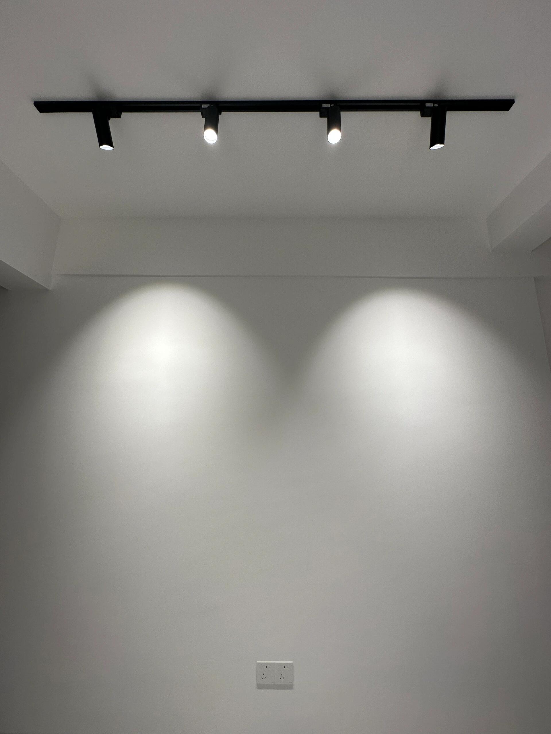 Black track light creating beautiful oval light wash patterns on white wall in minimalist studio - the small hill effect