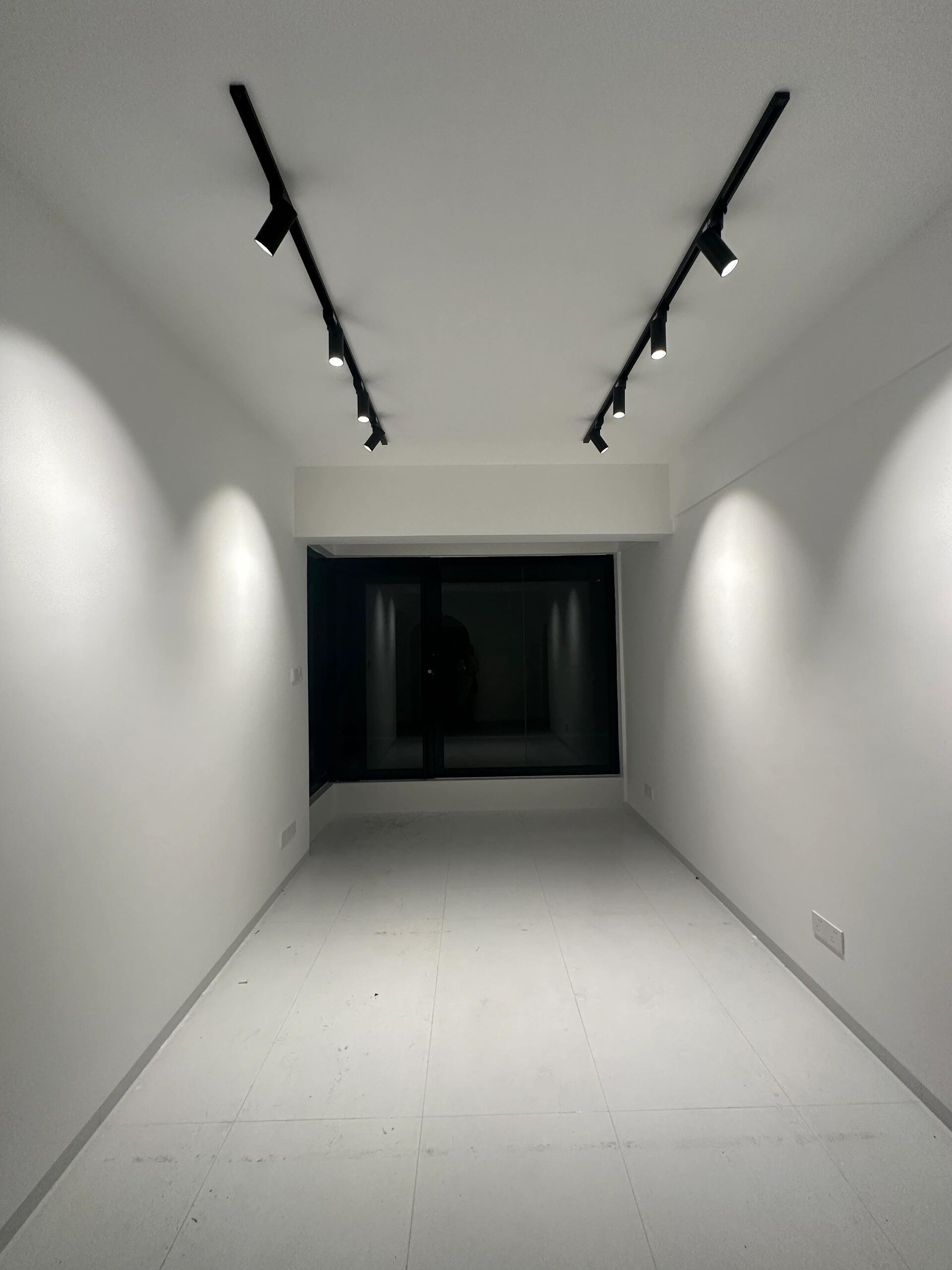 Full corridor view of dual V-arranged black track lights with 8 spotlights creating symmetrical gallery-style wash from near to far