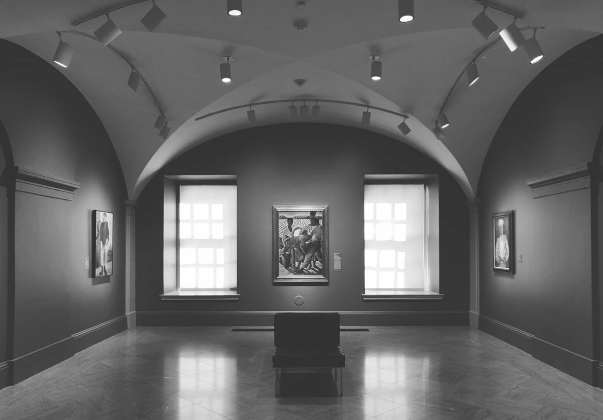 Vaulted gallery with track lighting heads on ceiling-mounted rails aimed at paintings on a dark wall