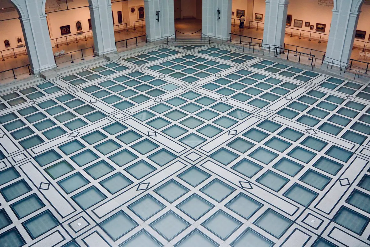 Beaux-Arts museum court in New York with daylight falling through a glazed floor structure onto stone columns