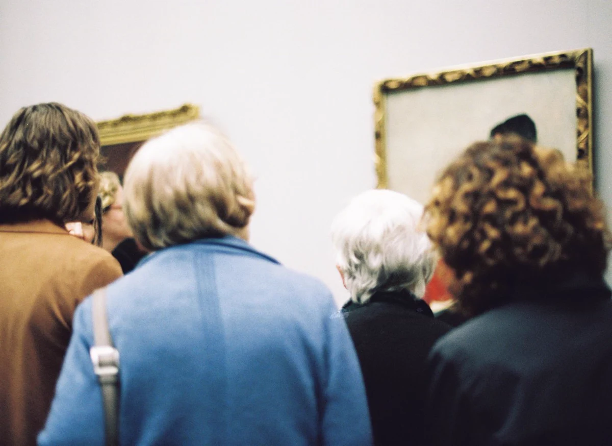 Visitors standing close to oil paintings in a museum gallery under low-glare track lighting