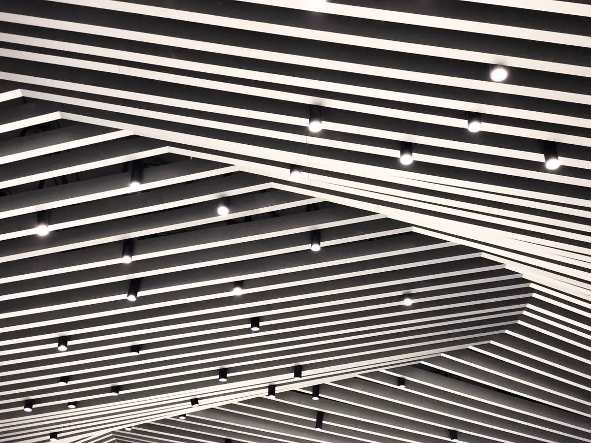 Museum ceiling with white acoustic baffles and surface-mounted track heads and spotlights in a dark grid