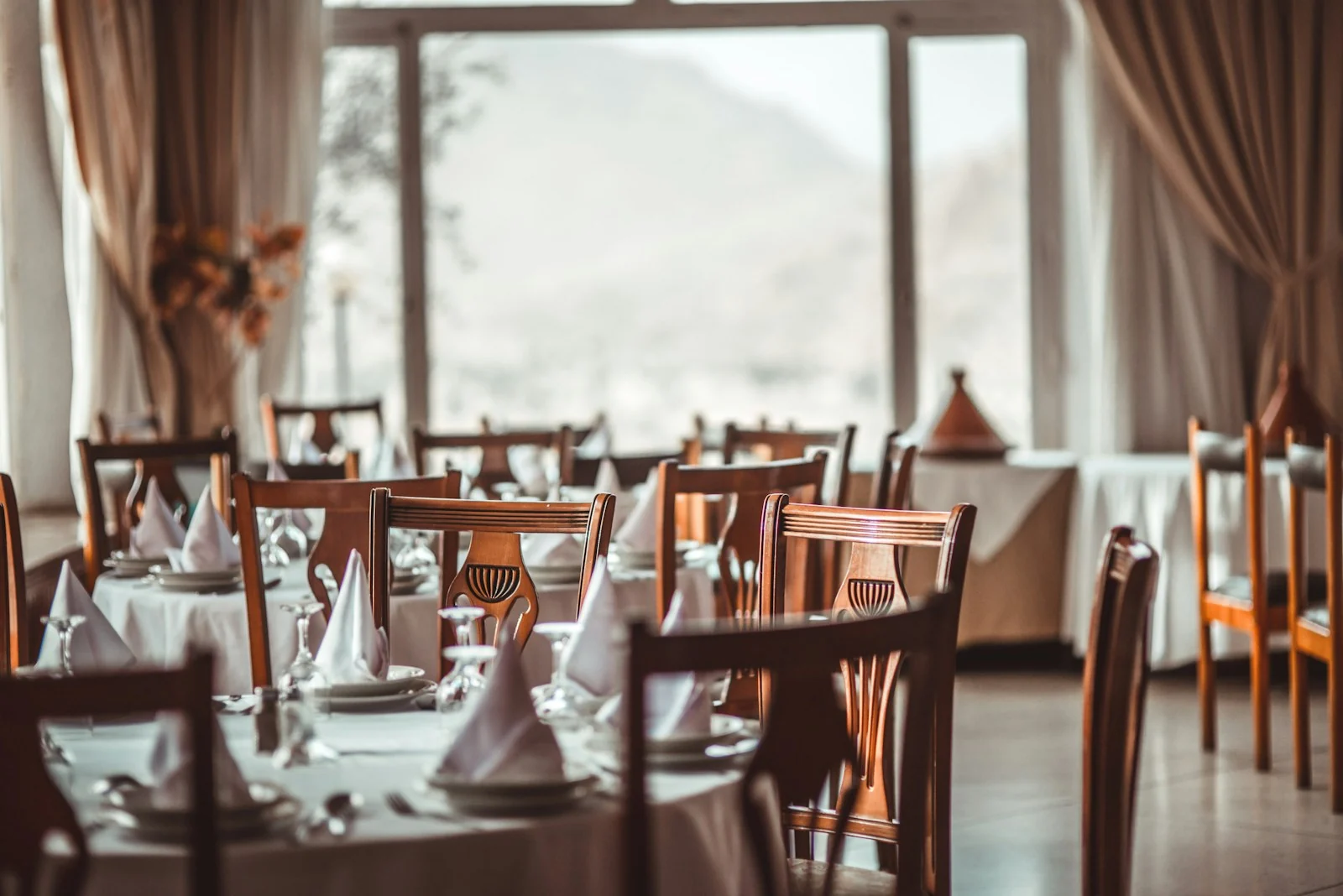 Luxury restaurant dining room with white linen tables and warm pendant lighting at 2700K in a fine dining setting