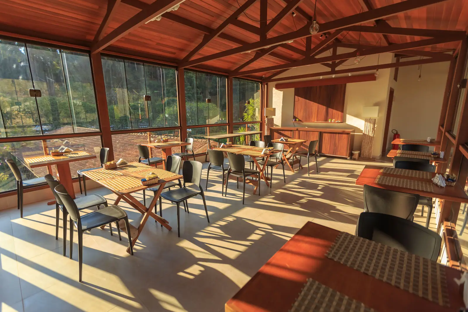 Restaurant dining hall with wooden tables and chairs lit by warm track and pendant lighting, showing an accent pool on each table against a softer ambient level
