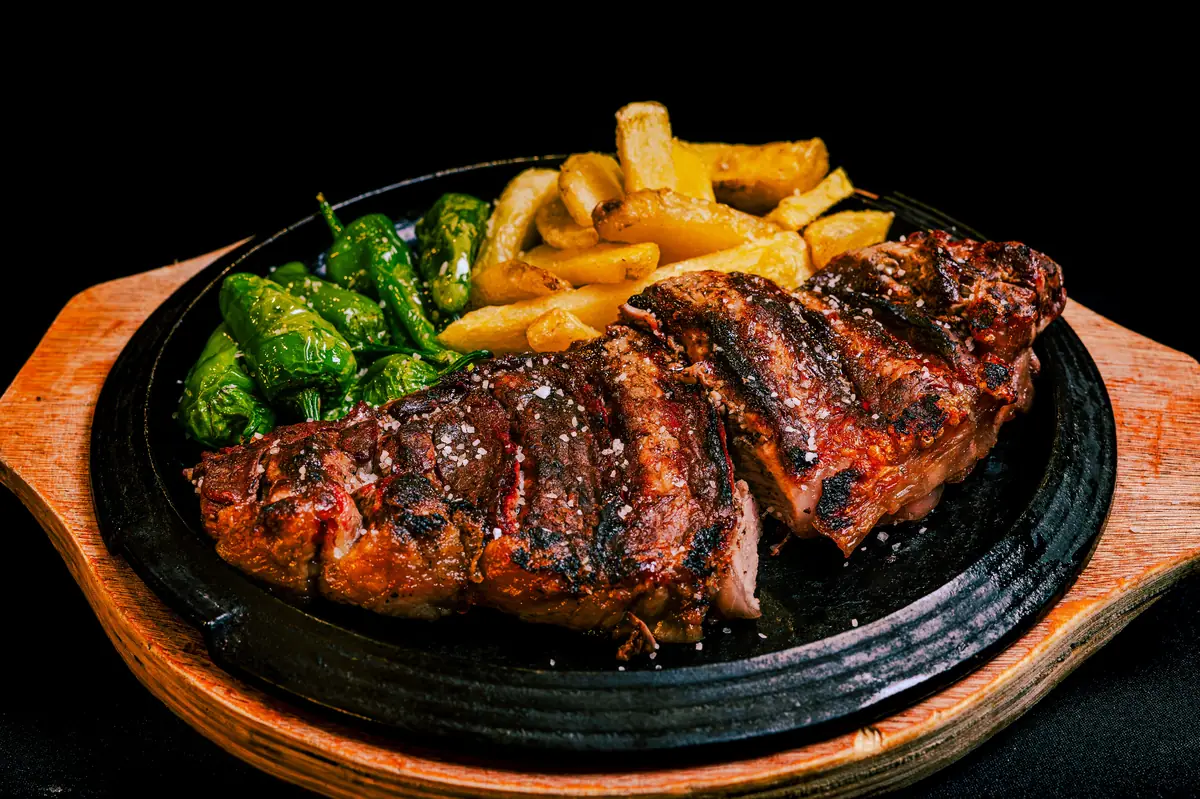 Grilled steak plated with fries and green peppers under warm restaurant lighting, showing the saturated red rendering that depends on R9 above 80