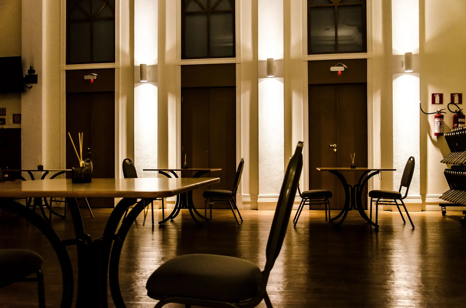Warmly lit restaurant dining room with chairs and tables under a low ambient level, showing the accent-to-ambient contrast that separates a designed room from a canteen