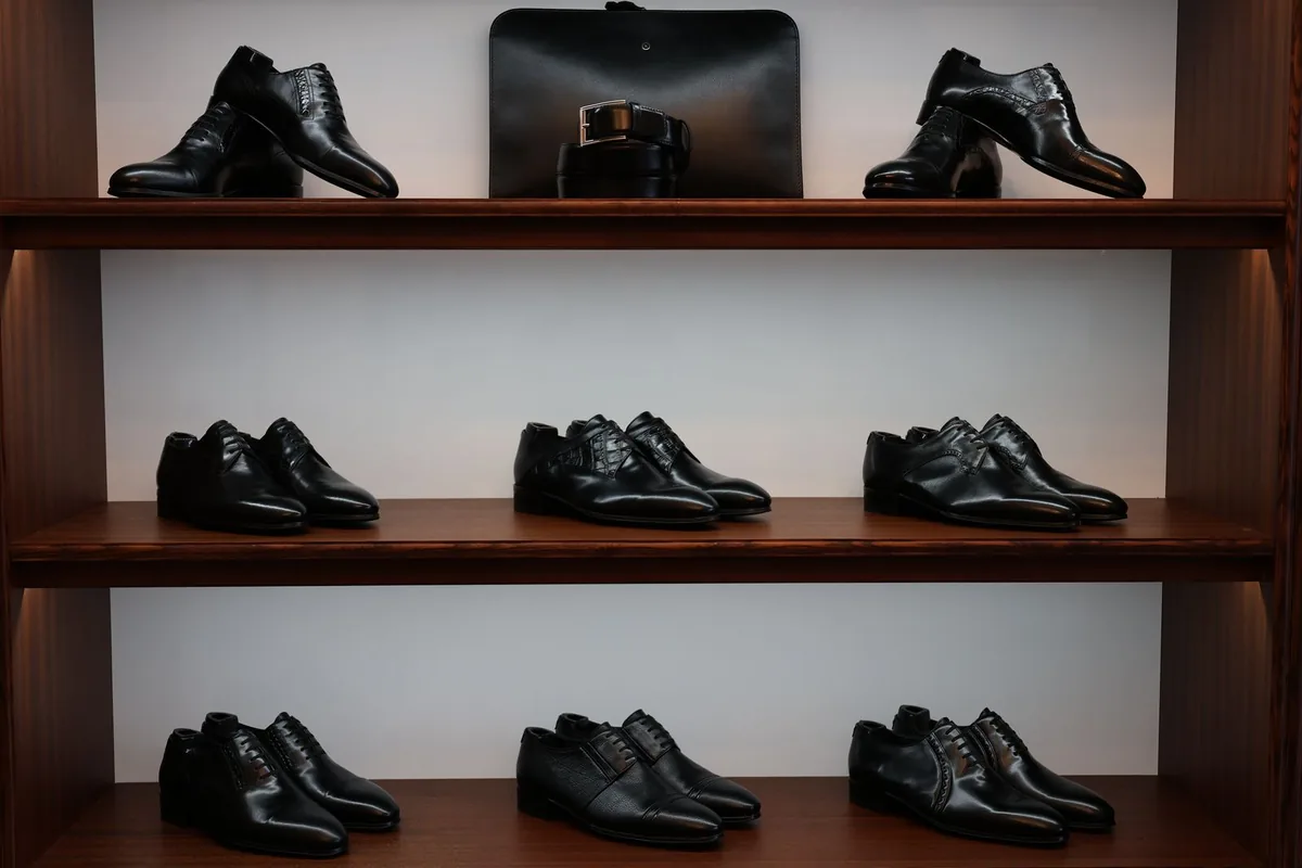 Black leather shoes on wooden retail display shelves lit so each shelf level reads clearly, an example of layered retail display lighting