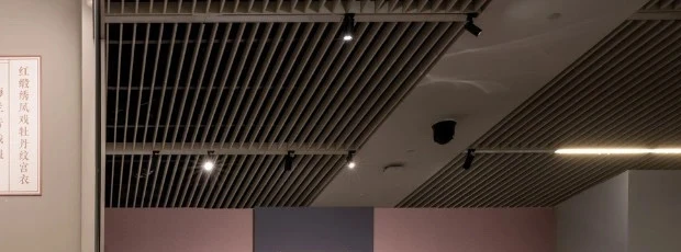 Close-up of a continuous white track rail and a slim linear light recessed between aluminium ceiling baffles in a completed showroom fit-out