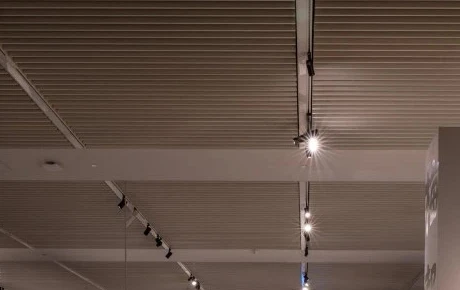 Track heads on a slim rail visible between horizontal ceiling baffles, aimed down a showroom aisle with heads parked and aimed individually along the run