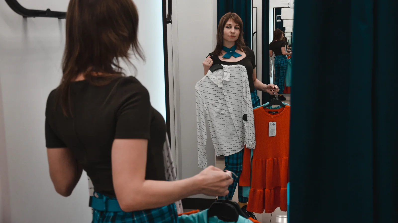 Customer standing in front of a fitting room mirror checking a garment, viewed from behind