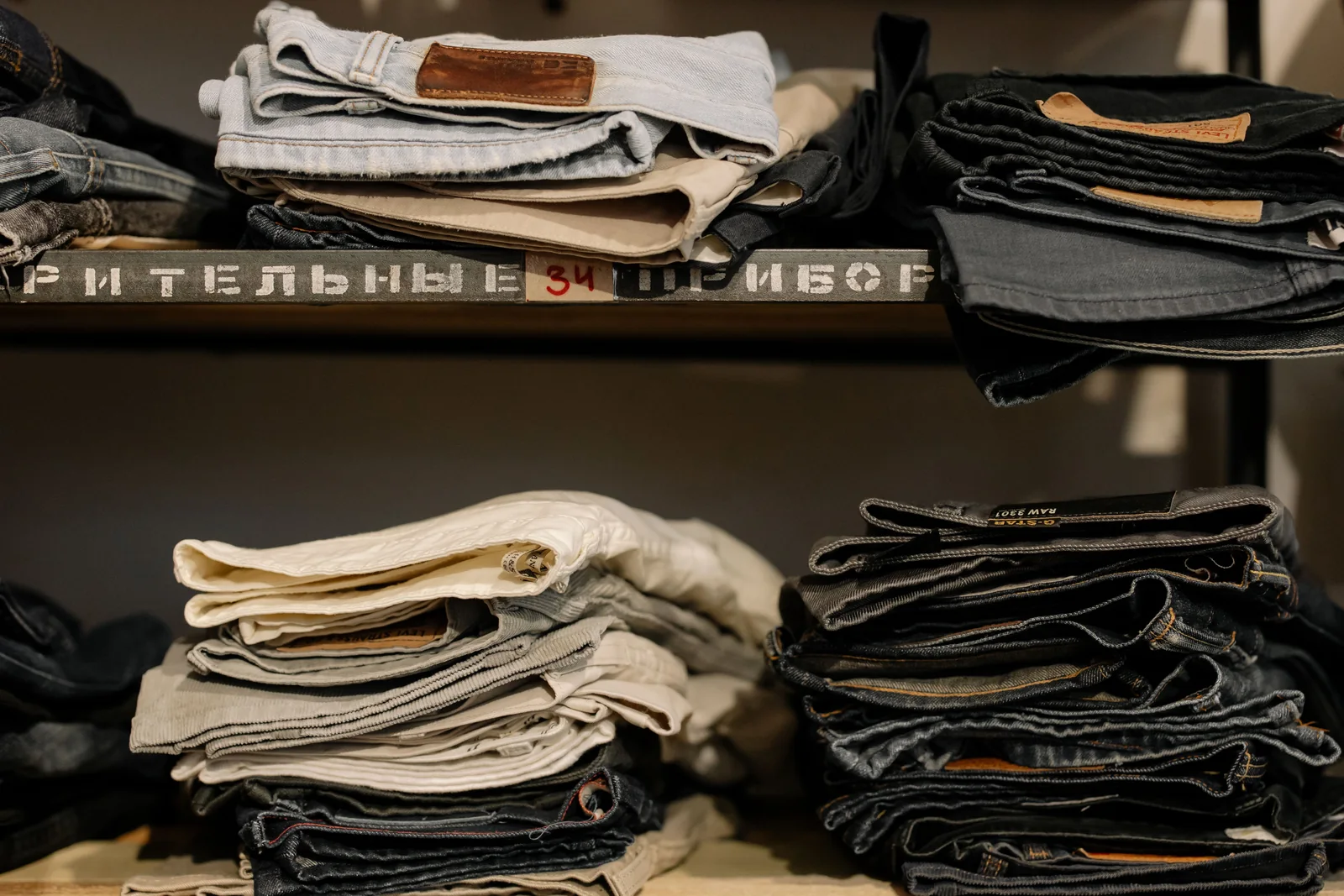 Folded denim jeans stacked on retail shelves lit from above with a controlled beam showing contrast between shelf levels