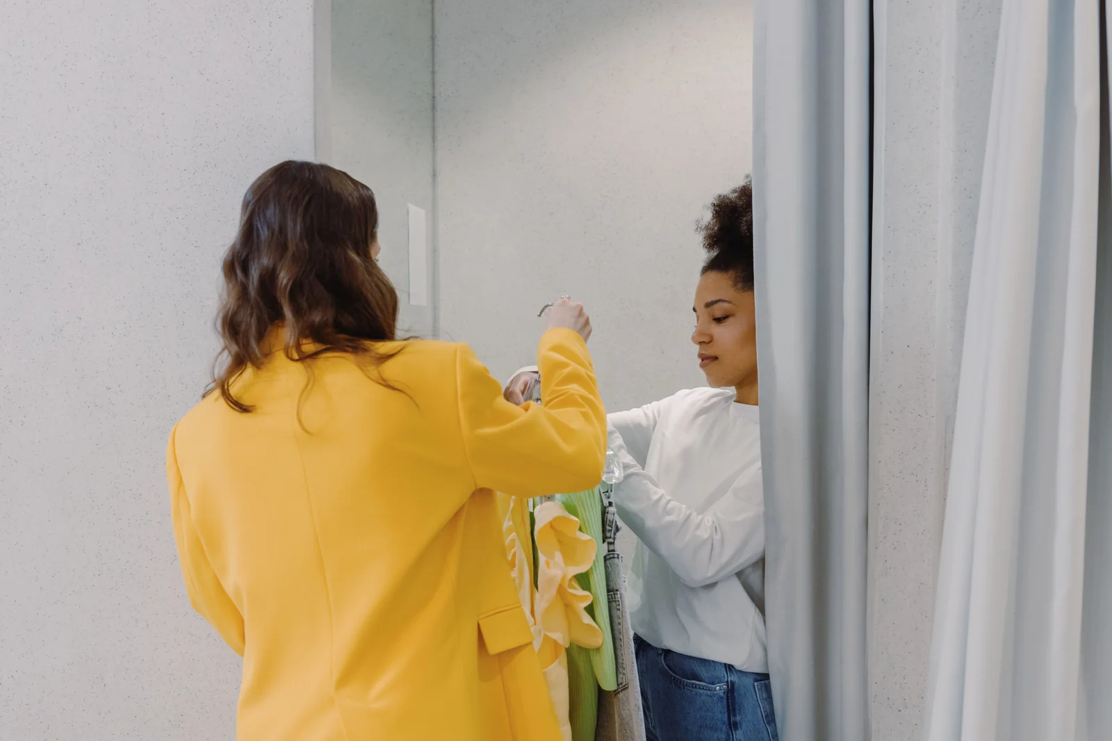 Stylist assisting a customer at the fitting area with garments held up in front of a mirror