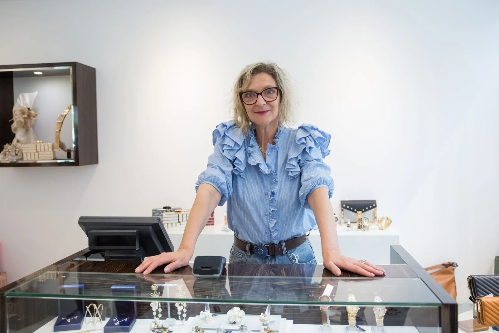 Sales associate standing behind a lit glass jewelry counter in a bright boutique with display cases on both sides