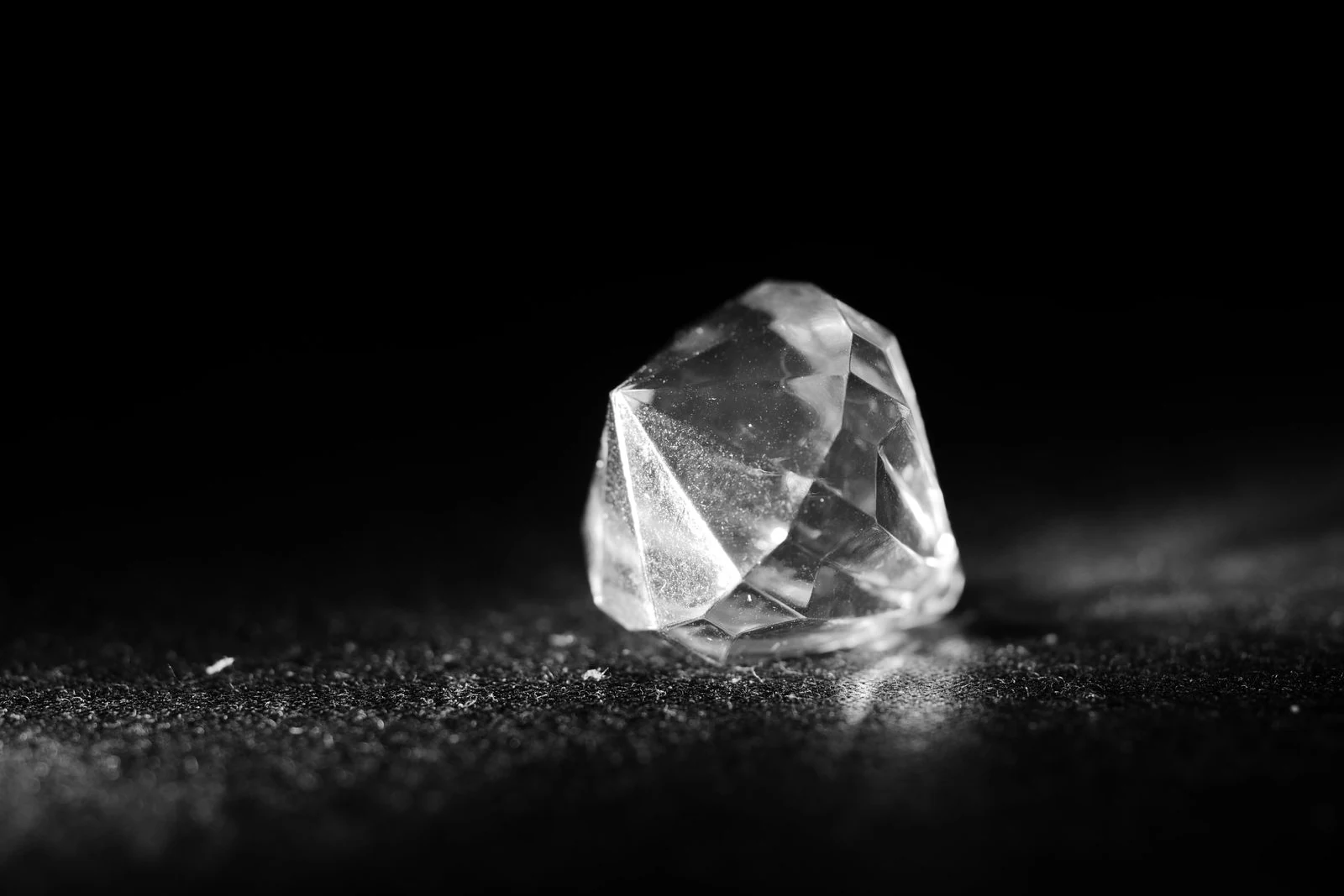 Macro photograph of a single cut diamond on a dark surface showing the facets and internal reflections that jewelry store lighting is meant to reveal