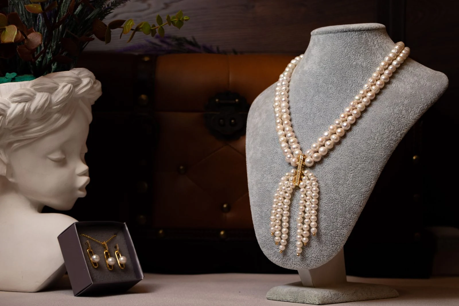 Pearl necklace on a grey display bust in a retail case, illustrating the vertical presentation that jewelry store lighting must render at high colour fidelity
