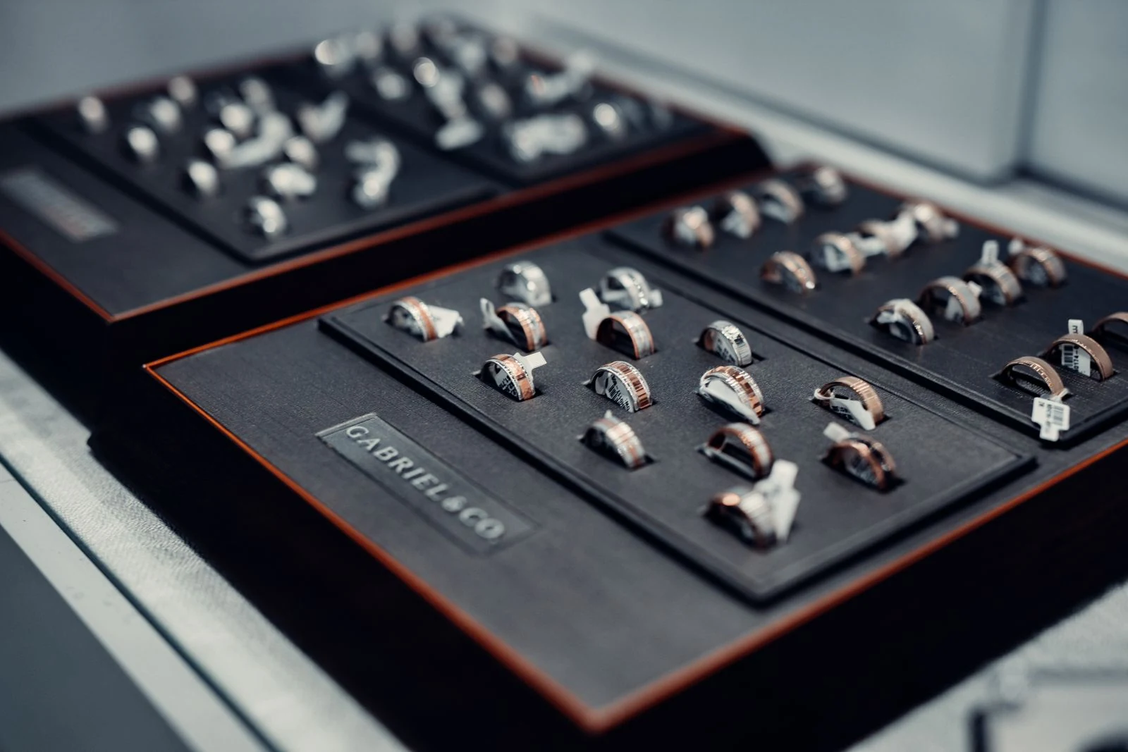 Silver and diamond rings on dark velvet display trays inside a jewelry store case under directional spot lighting that reveals high polish and fine detail