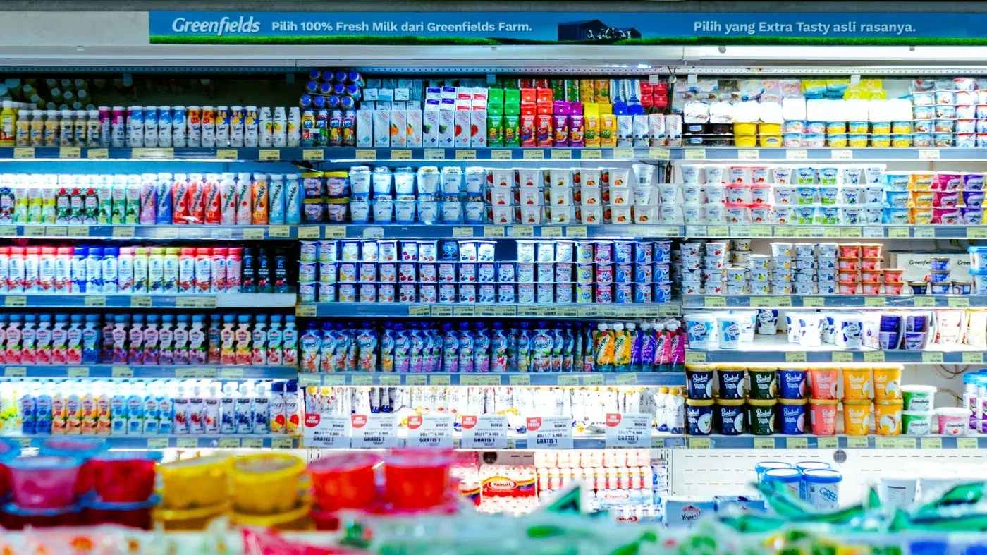 Chilled dairy and drinks cabinets in a supermarket under cool white lighting, showing the shelf face behind glass doors that track heads must not aim at normal incidence