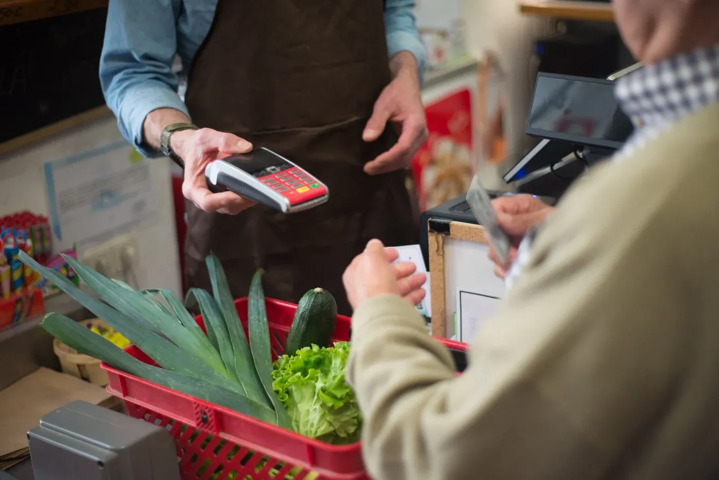 Supermarket checkout counter with a customer paying and fresh produce in a basket under bright 500 to 750 lux lighting